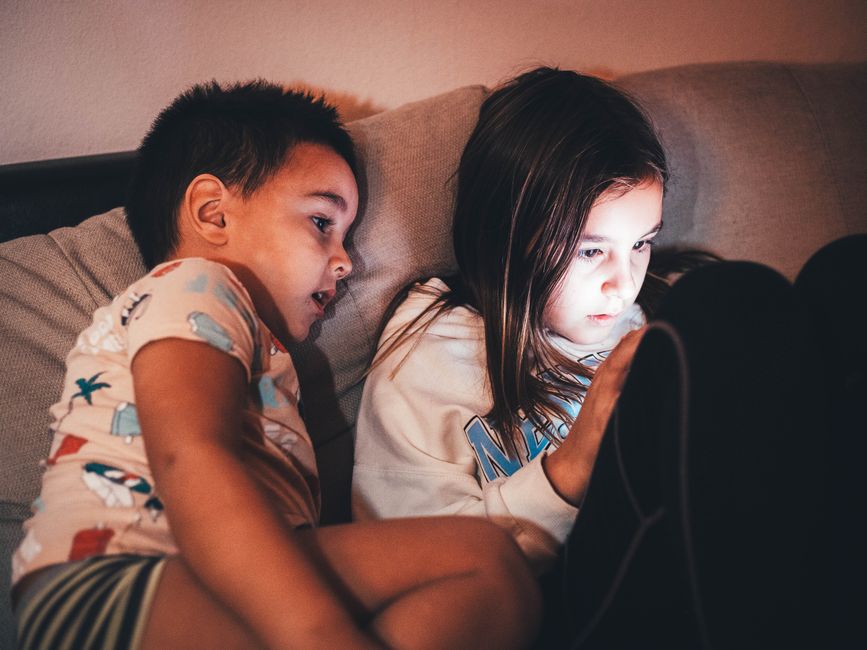 Photo by Boris Hamer on Pexels Two children relax on a couch, absorbed in a glowing tablet screen. - Photo by Boris Hamer on Pexels