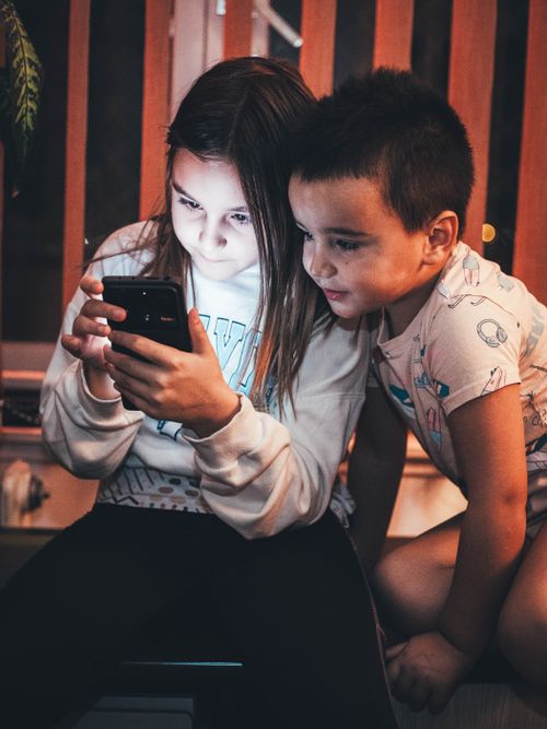Free Two children captivated by a smartphone screen indoors, creating a cozy and engaging atmosphere. Stock Photo