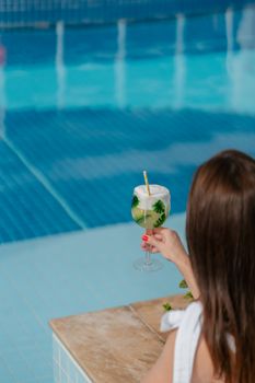 Adult woman enjoying a refreshing cocktail by a swimming pool, capturing a relaxed summer vibe.