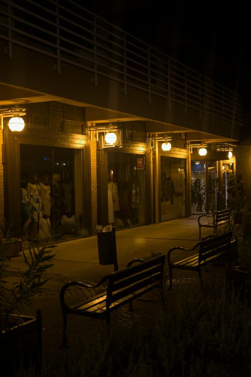 Free A dimly lit shopping arcade with benches and lit storefronts during a dark night. Stock Photo
