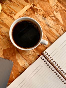 A cup of black coffee next to a notebook on a textured wooden table.