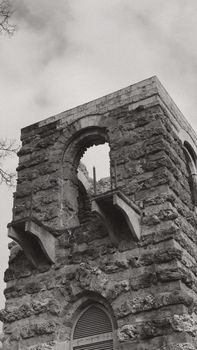 Black and white image of a historic stone tower with an arch and an overcast sky.