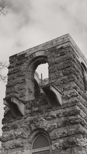 Fotomural Imagen en blanco y negro de una torre de piedra histórica con un arco y un cielo nublado.