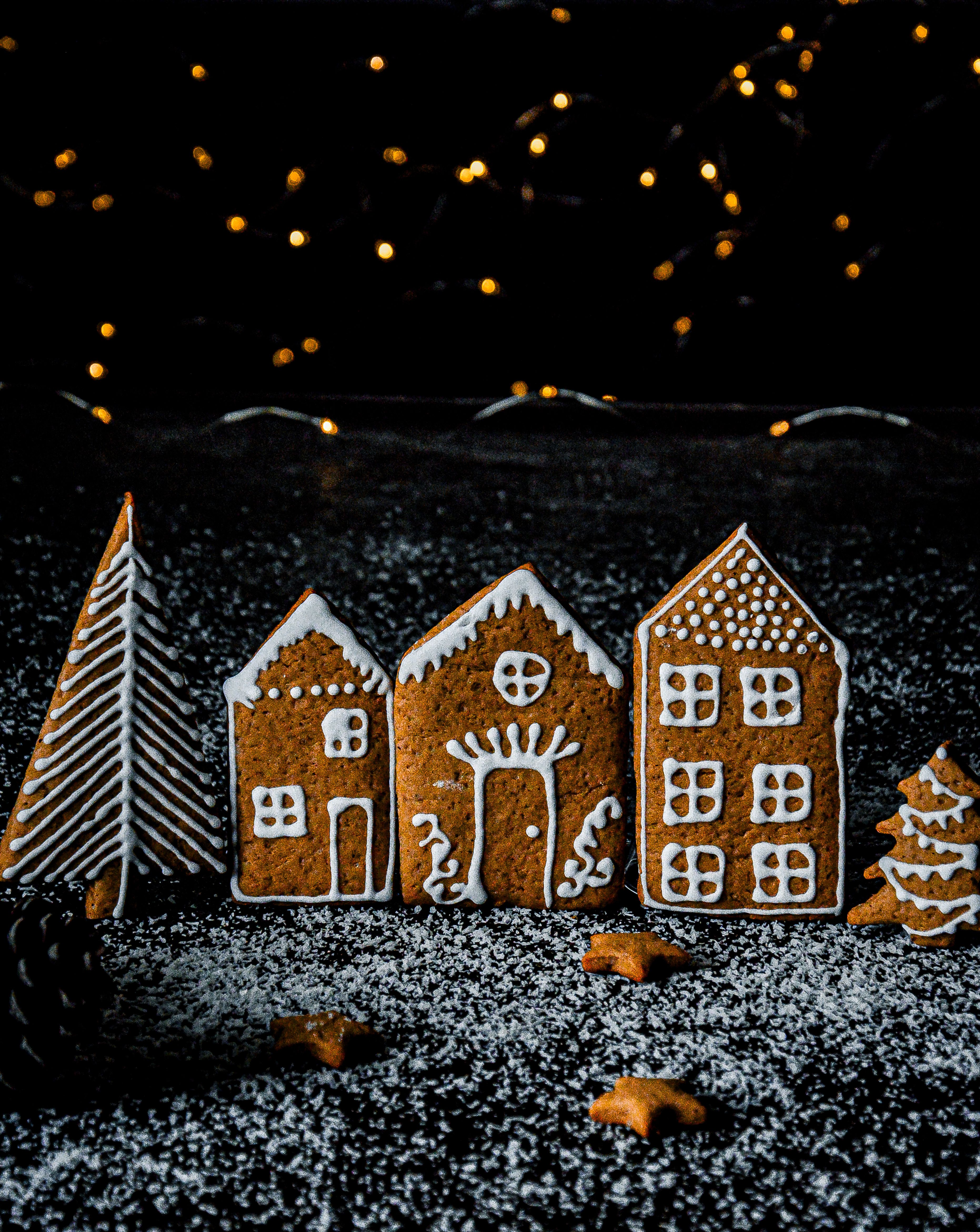 Three cozy gingerbread houses and trees with decorative icing against a backdrop of fairy lights.