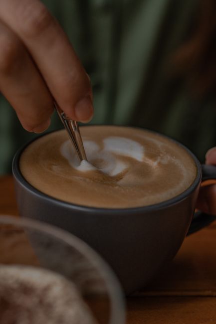 Close-up of a hand stirring latte art foam in a cup of coffee.