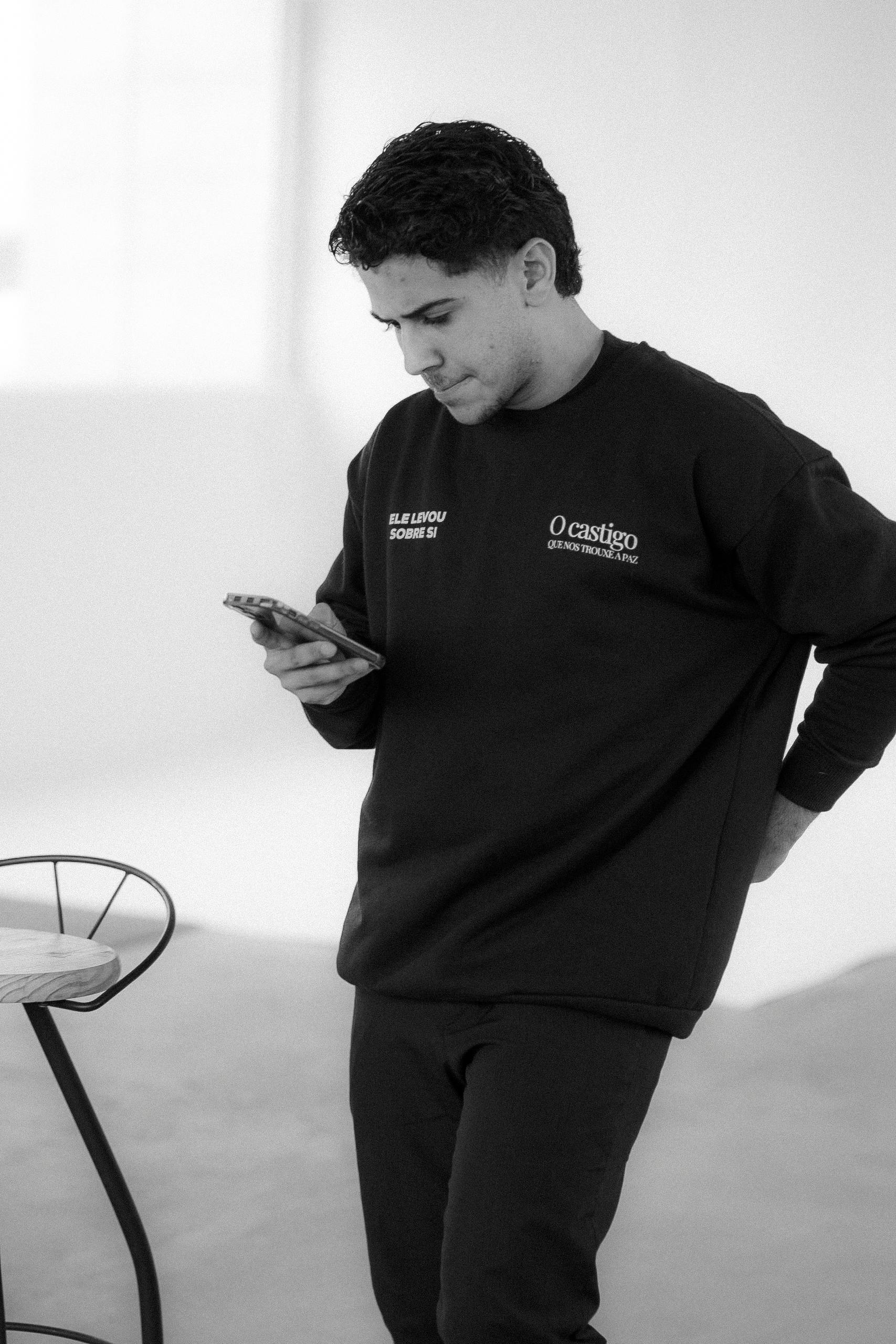 Ücretsiz Siyah, rahat bir kıyafet giyen genç adam, içeride akıllı telefonunu kullanarak modern yaşam tarzını sergiliyor. Stok Fotoğraflar