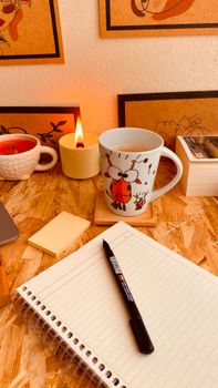 Warm and inviting desk setup with a hot beverage, candle, and notebook, perfect for studying or relaxing.