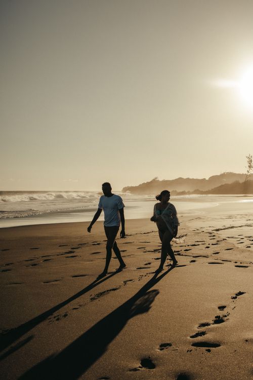 Free Silhouetted couple strolling along Saint-Denis beach at sunset with gentle waves and warm tones. Stock Photo