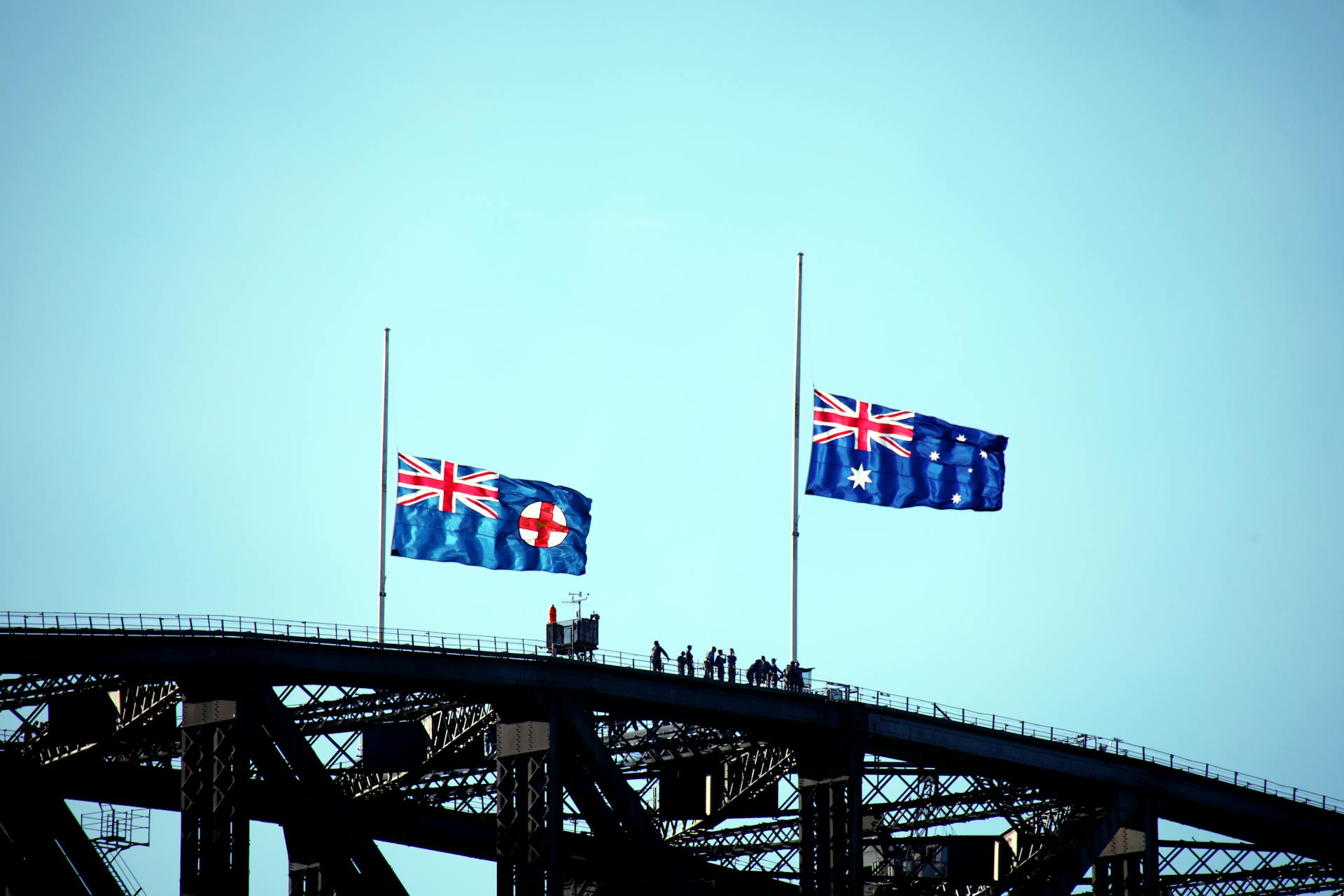 Australian and New South Wales flags flying on Sydney Harbour Bridge silhouette.