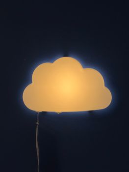 Warm cloud-shaped night light mounted against a dark blue wall, illuminating softly.