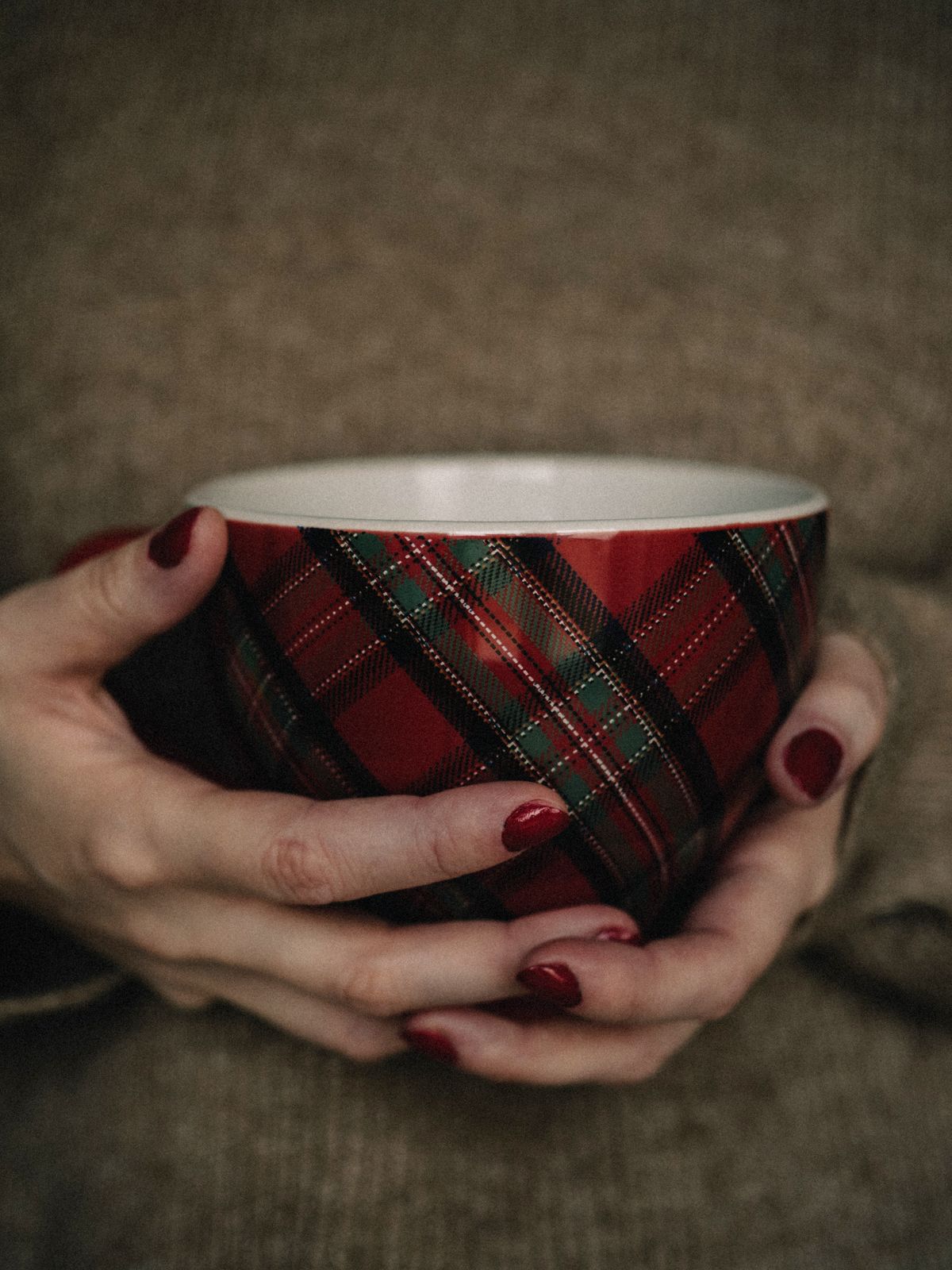 Close-up of hands holding a tartan patterned mug, evoking warmth and coziness indoors.