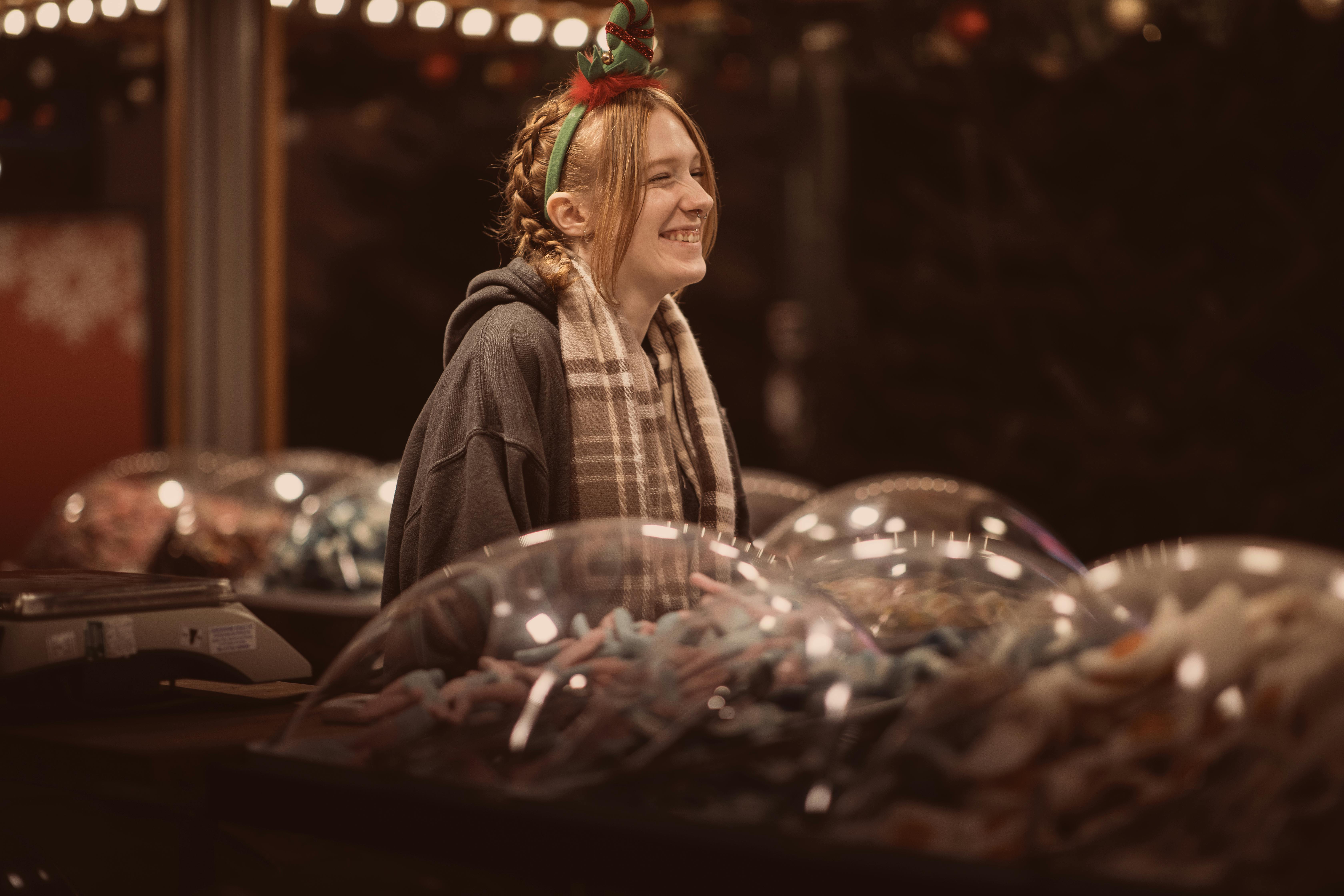 Vendor smiling at Bournemouth Christmas market, offering sweets in festive atmosphere.