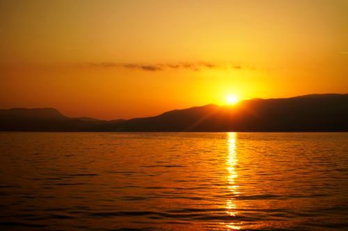 Free Stunning sunset reflecting over a tranquil lake with silhouetted mountains. Stock Photo