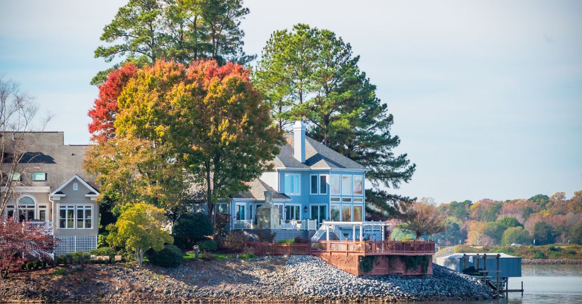 A picturesque lakeside house surrounded by colorful autumn trees by the water.