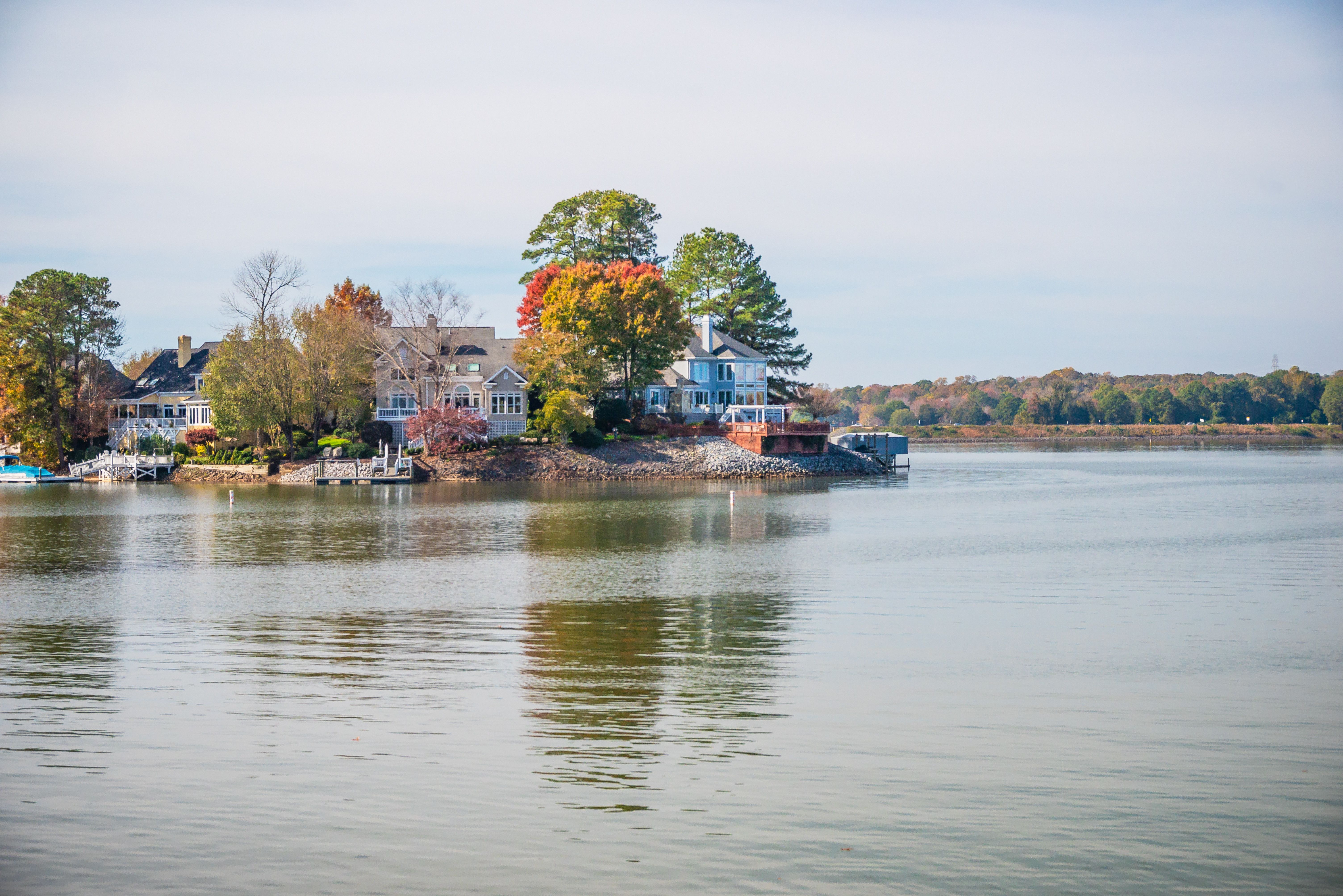 Beautiful lakeside houses surrounded by autumn trees and calm water reflecting the serene setting.