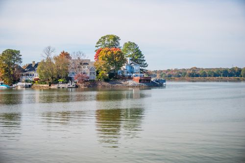 Free Beautiful lakeside houses surrounded by autumn trees and calm water reflecting the serene setting. Stock Photo
