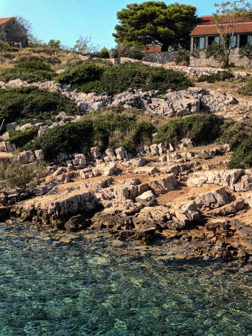 Free Beautiful rocky coast with clear turquoise waters and lush greenery in a serene setting. Stock Photo