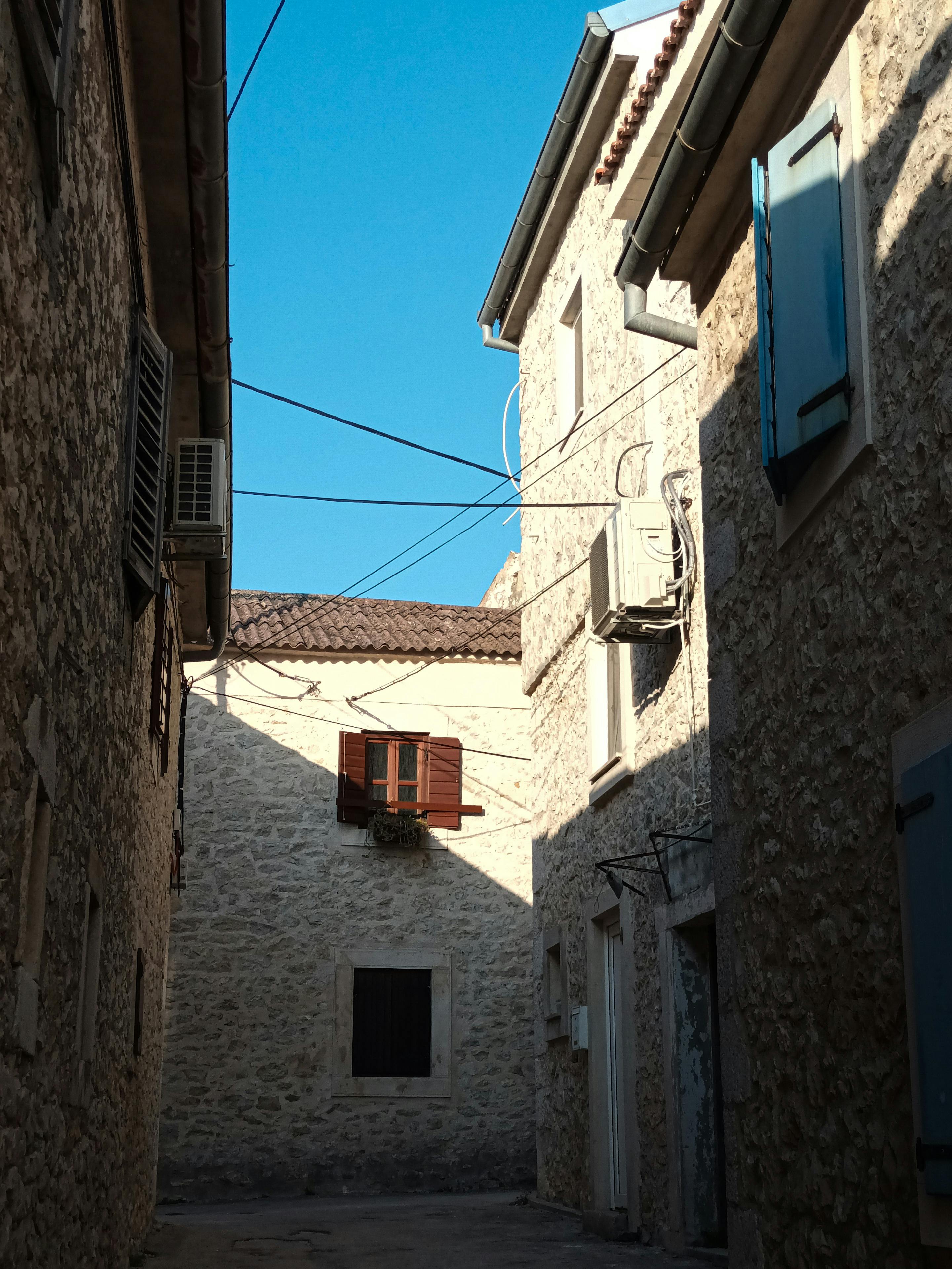 Quiet stone alleyway with rustic buildings under a clear blue sky.