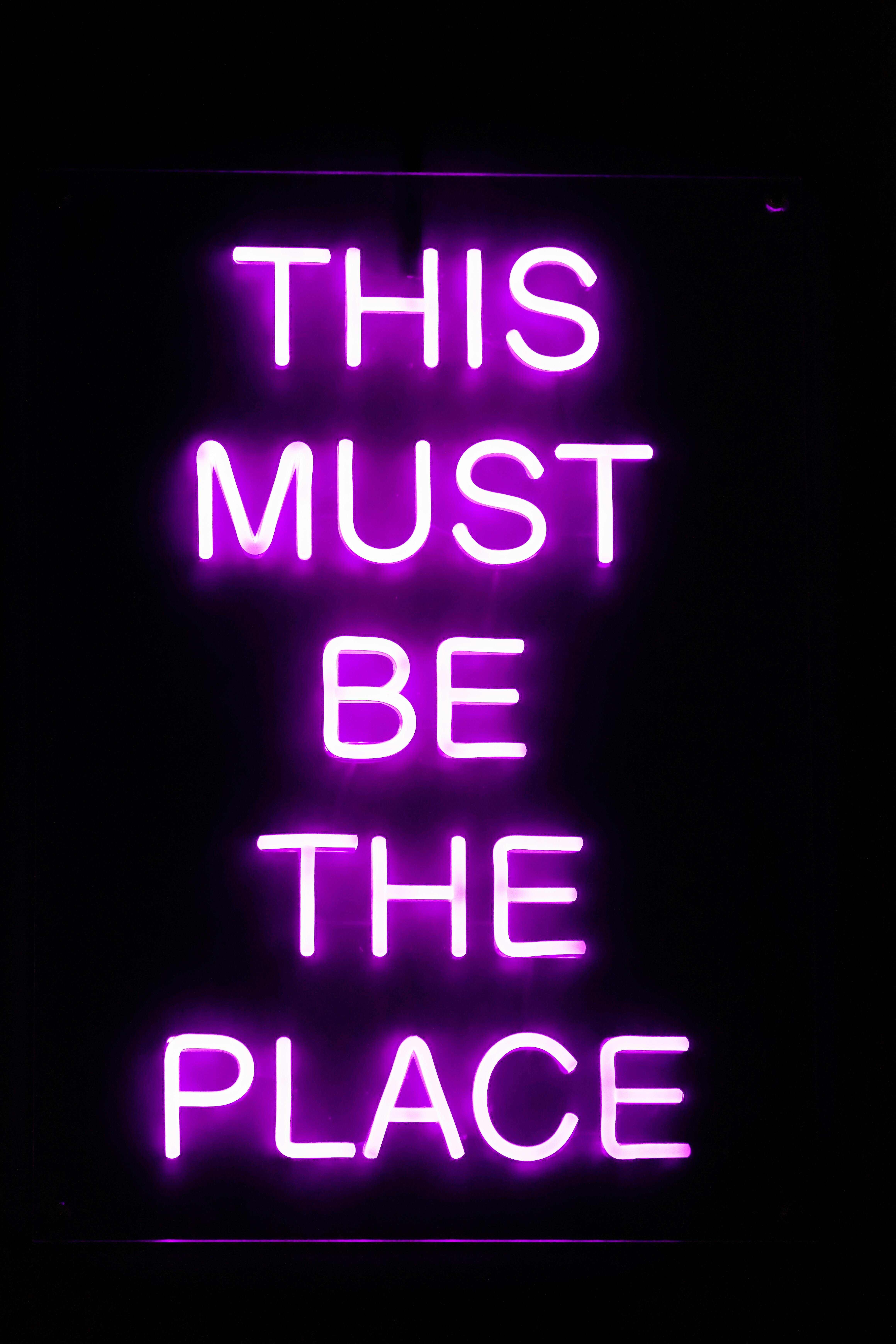 Gratis Tanda neon ungu terang yang menampilkan kata-kata 'Ini Pasti Tempatnya' dengan latar belakang gelap. Foto Stok
