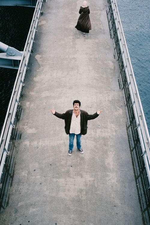 Free Man standing on a concrete bridge over water, arms open, urban setting Stock Photo