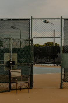 一个废弃的网球场，围着铁丝网，放着一把孤零零的椅子，透着平静
