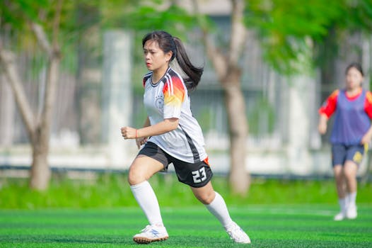 A young woman in a soccer uniform plays on a vibrant green field in Hanoi, Vietnam.