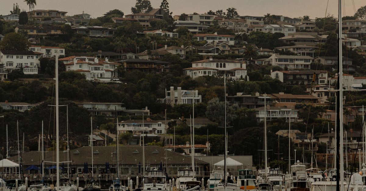 A tranquil marina with boats docked against a backdrop of charming hillside homes.