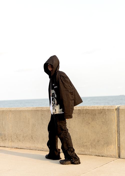 Free A person in a hooded jacket walking by a concrete sea wall, casting a mysterious vibe. Stock Photo