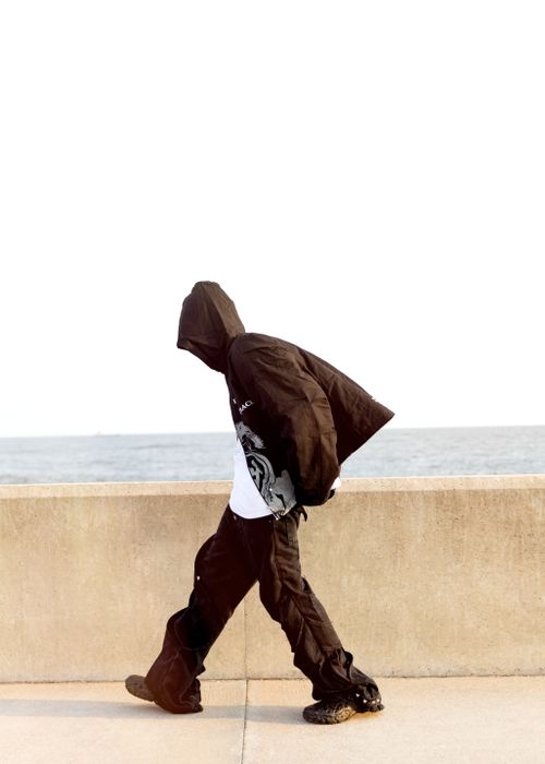 Free A person in a hooded jacket and fashionable pants walks by the seaside. Stock Photo