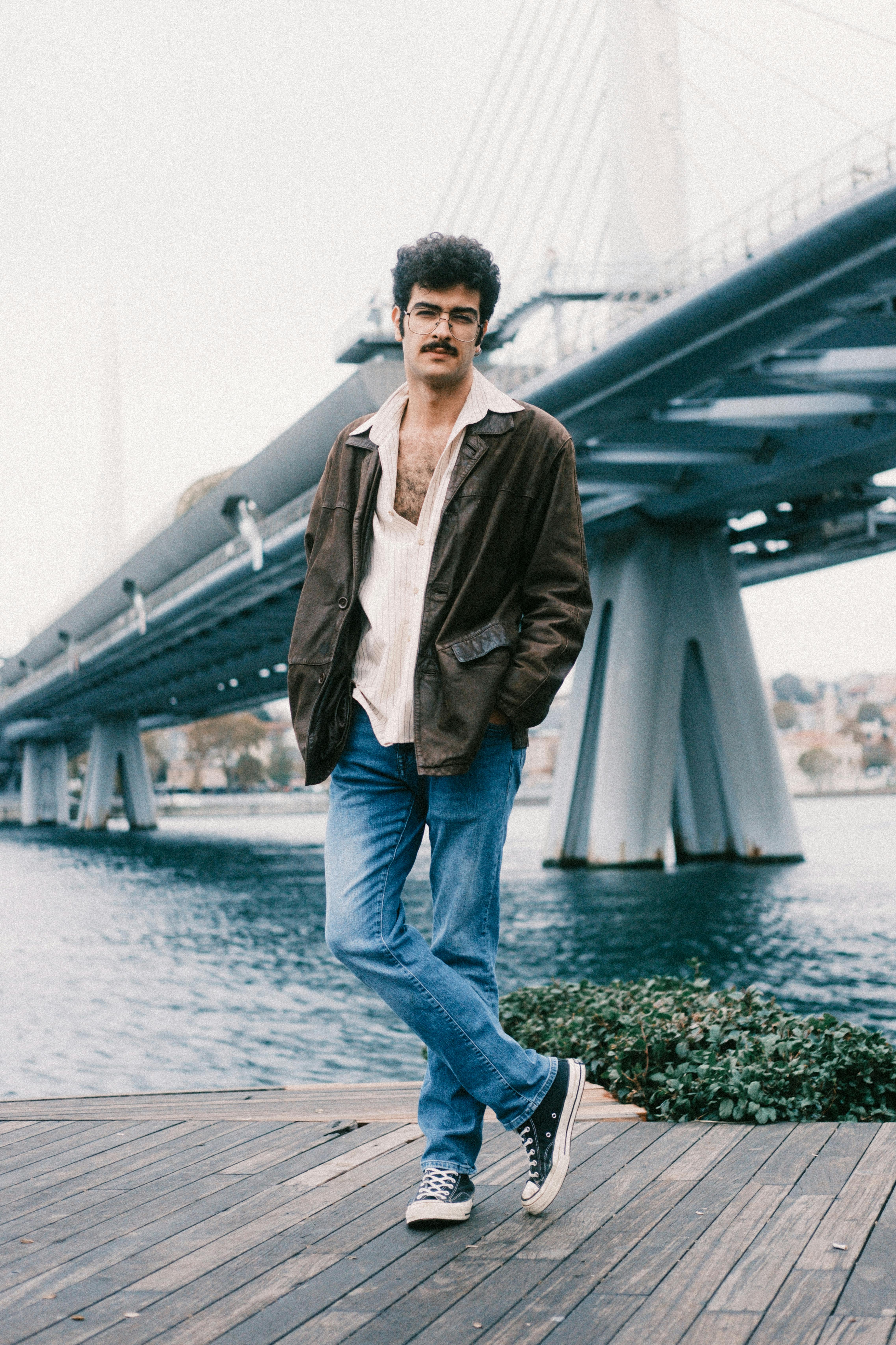 Casually dressed man posing by a modern bridge, reflecting an urban lifestyle.