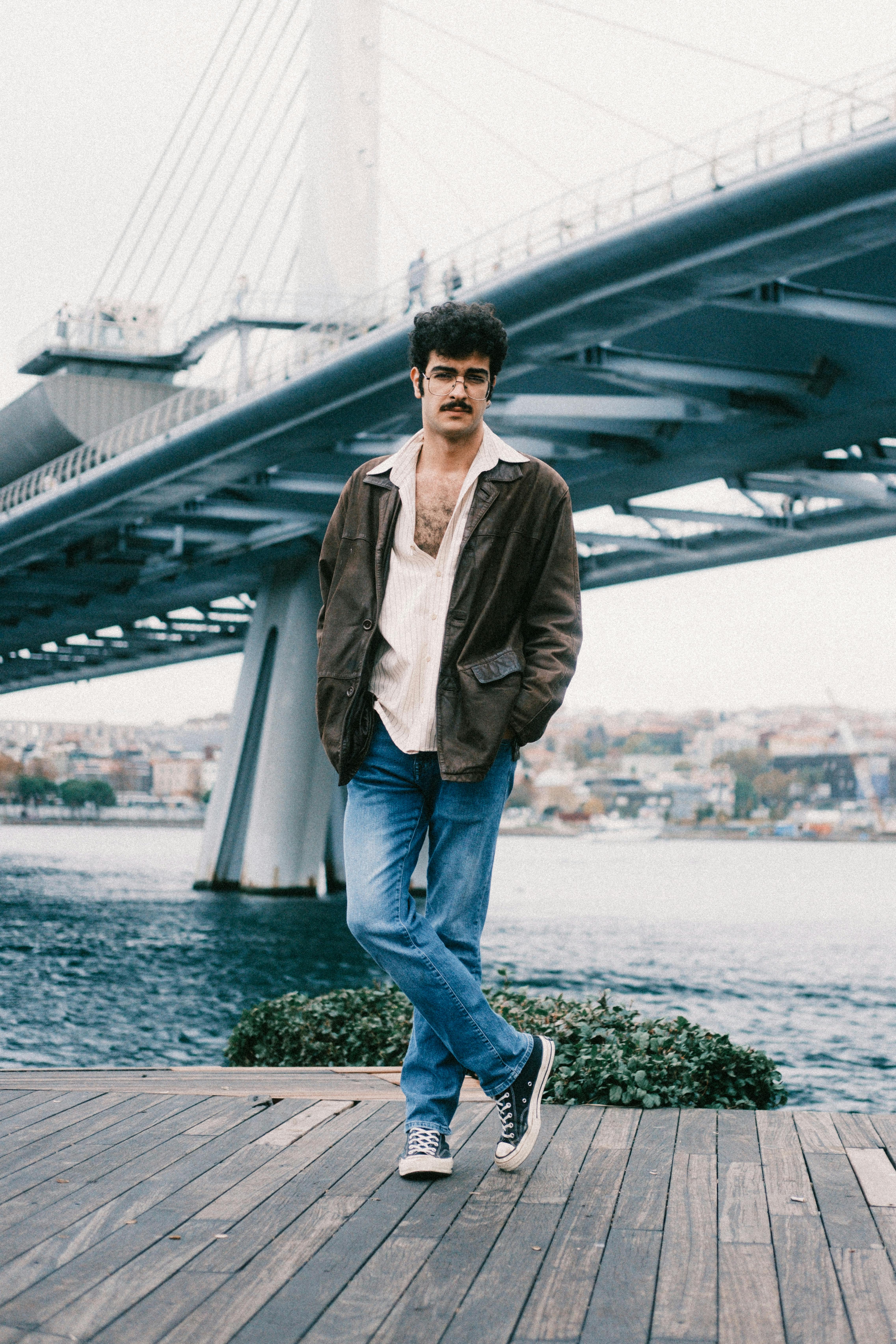 Stylish man leaning against railing with iconic modern bridge in background.