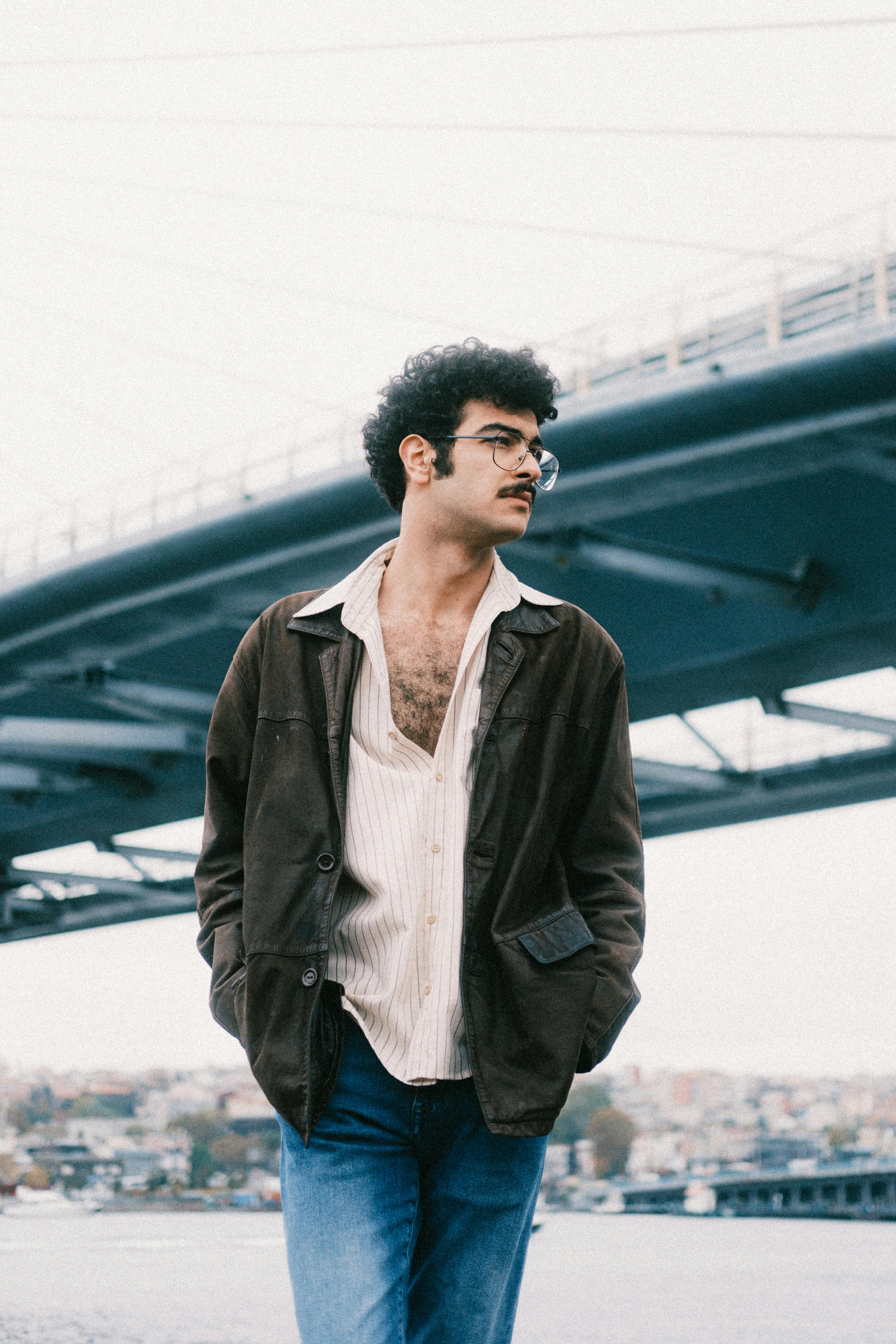 Young man standing stylishly under an urban bridge with a contemplative look.