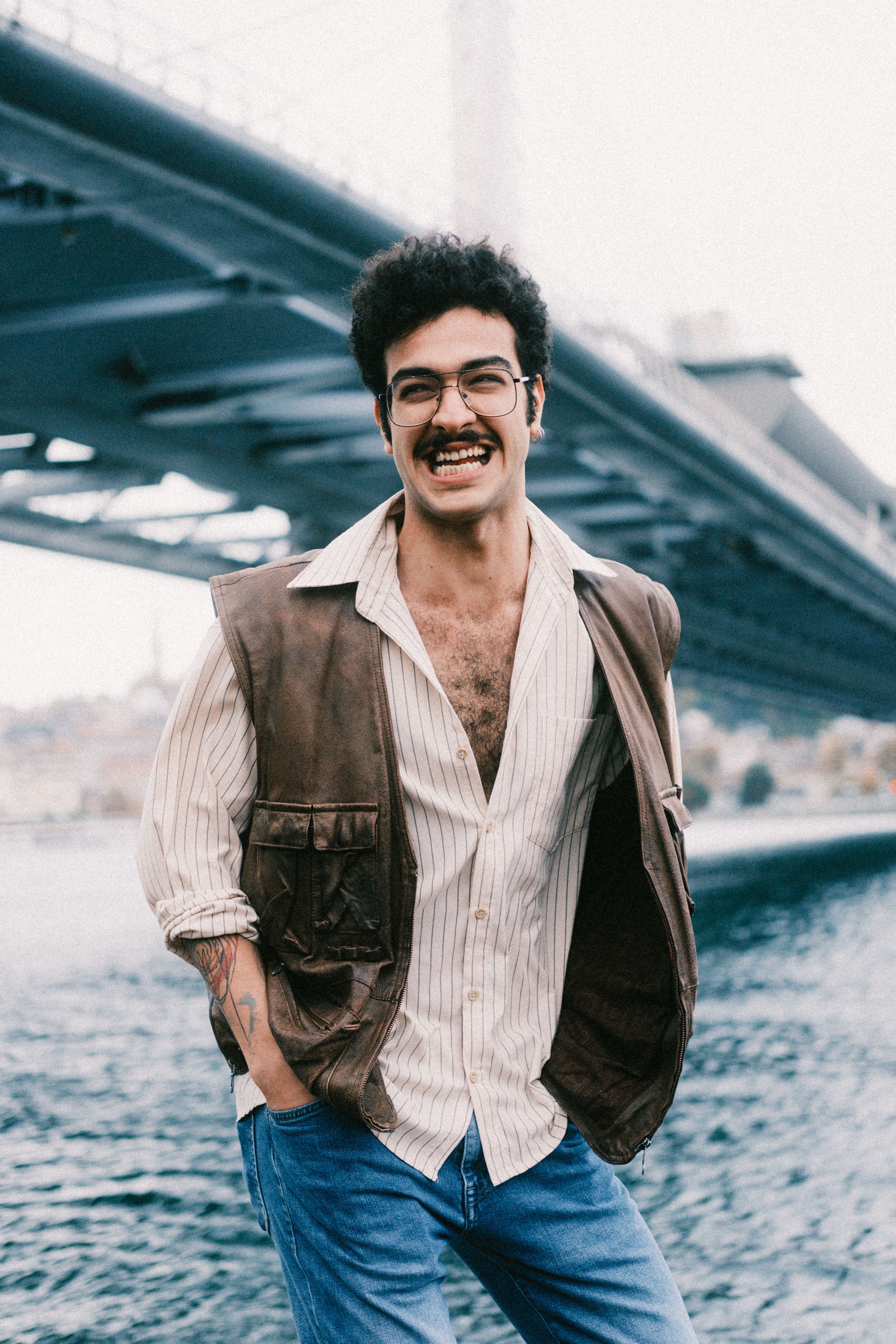 A cheerful man with a mustache standing under a bridge by the river.