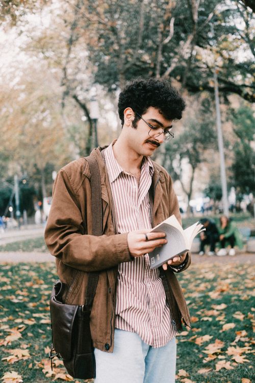 Free Young man reading a book in a serene autumn park setting with fallen leaves. Stock Photo