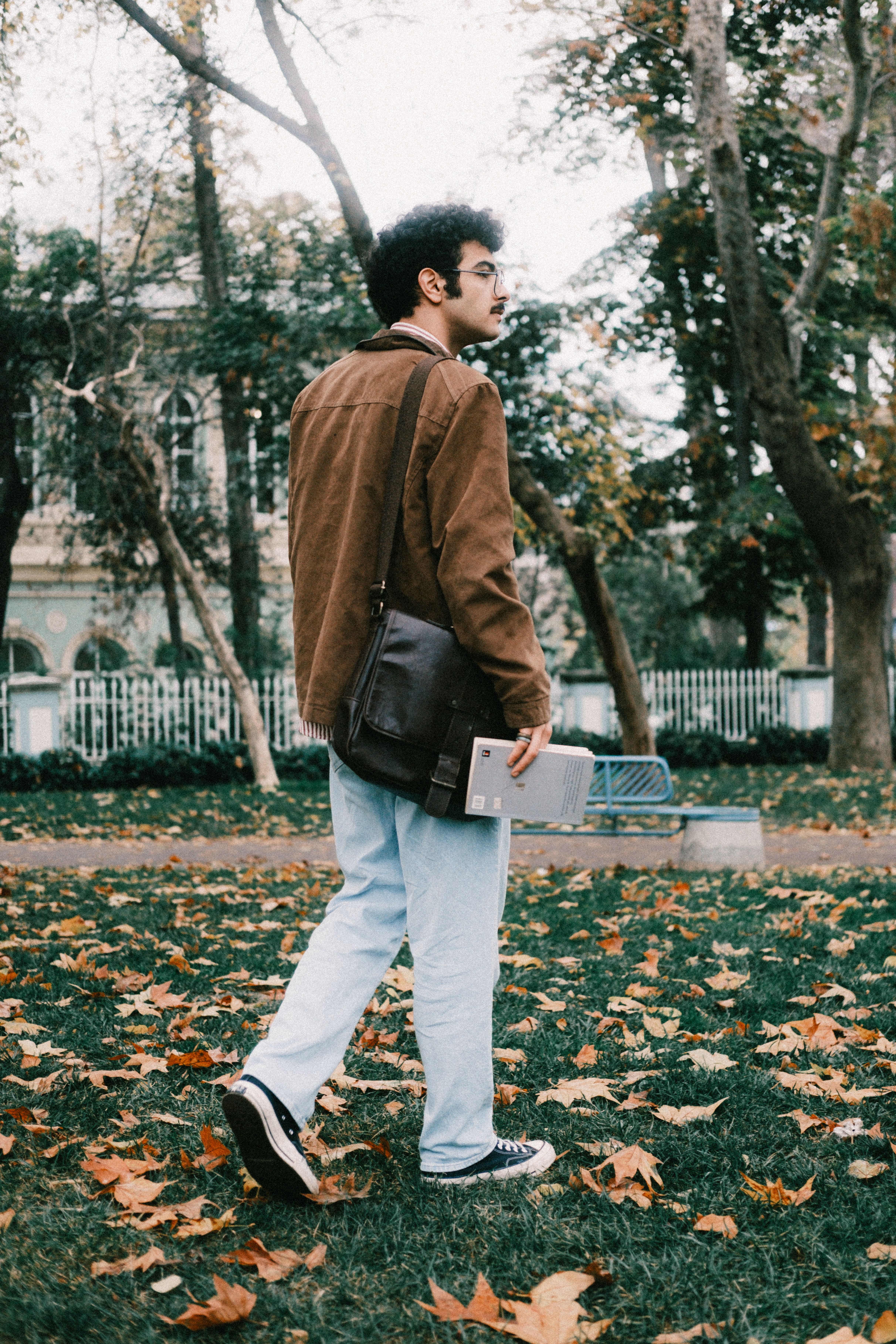 Young man walking through autumn park with books