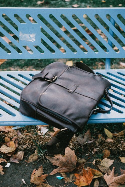 Free Brown leather messenger bag on blue bench with autumn leaves. Stock Photo