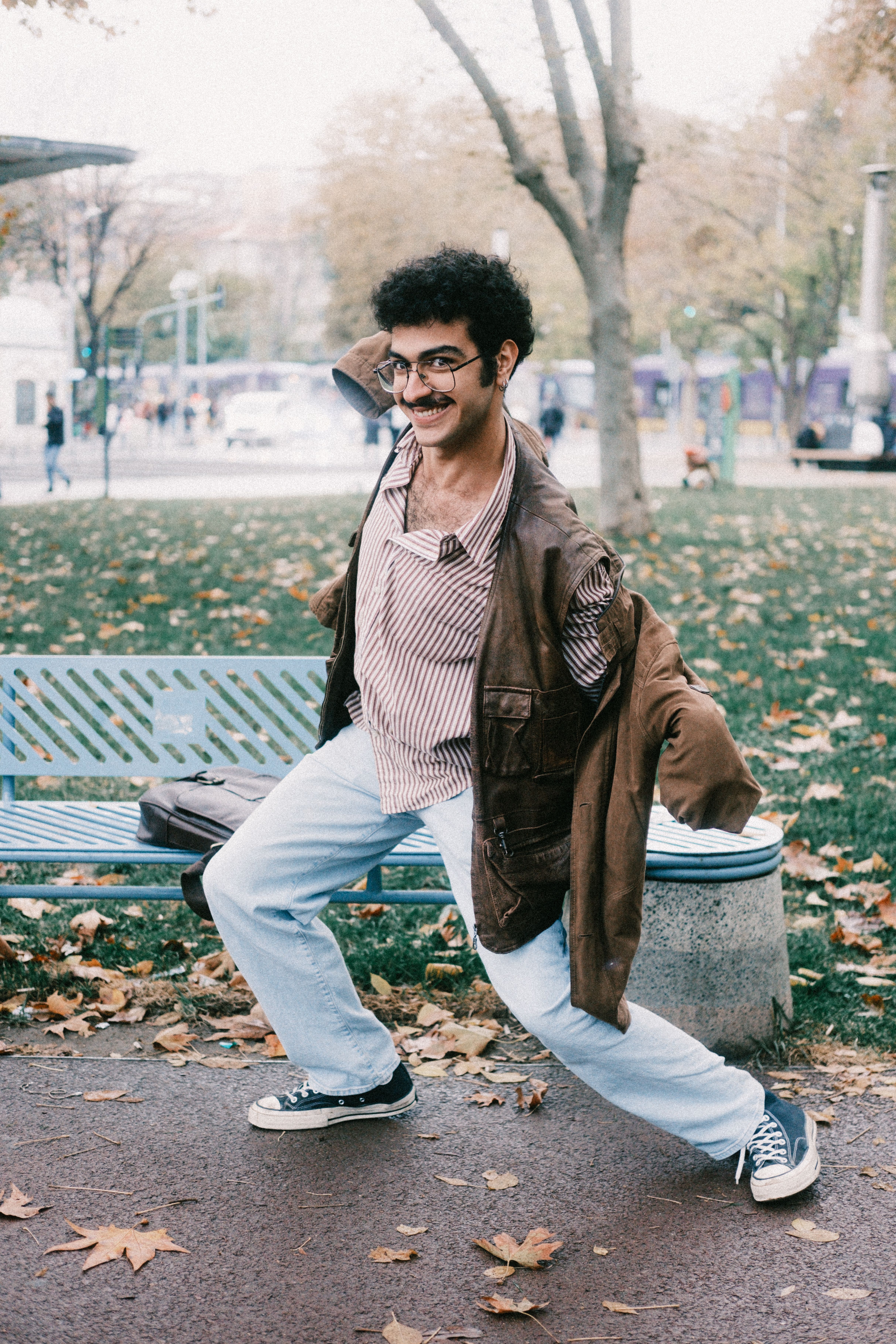 Young man striking a playful pose in an autumn park setting.