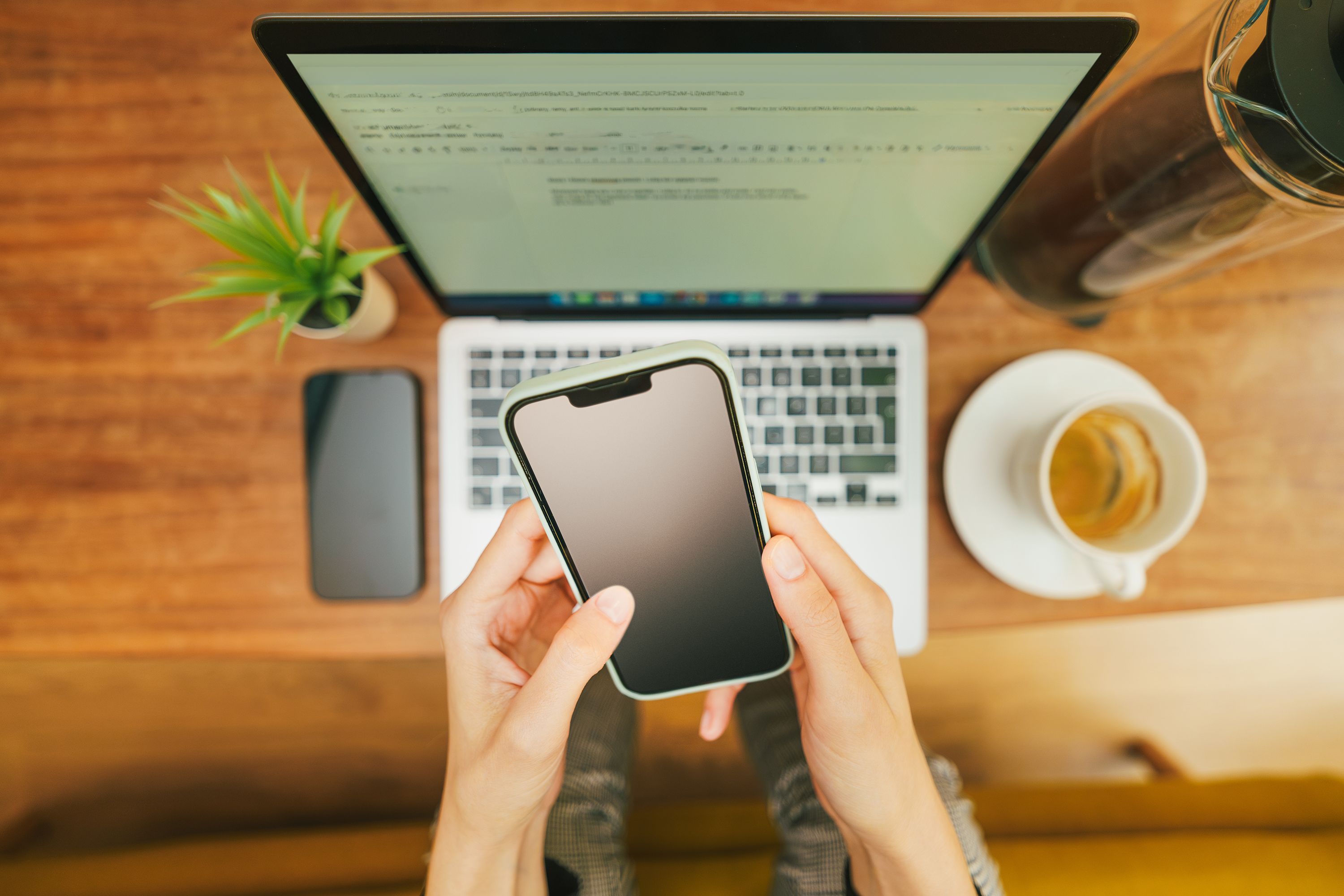 Profissional usando smartphone diante de um laptop em ambiente de trabalho