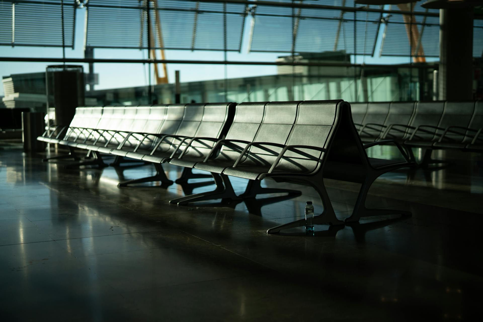 Deserted airport seating area with sunlight streaming through large windows. Calm and quiet atmosphere.