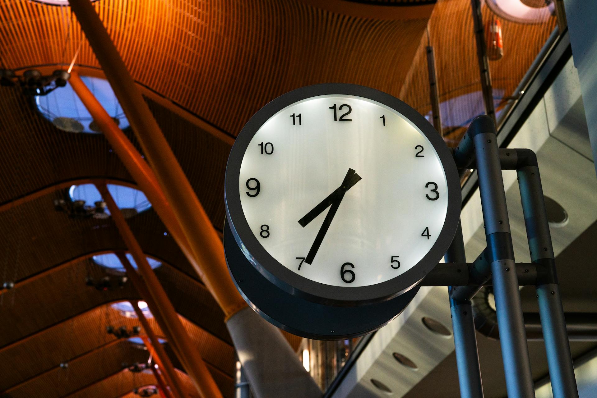 A large clock displaying one o'clock inside a modern airport terminal with a curved ceiling.