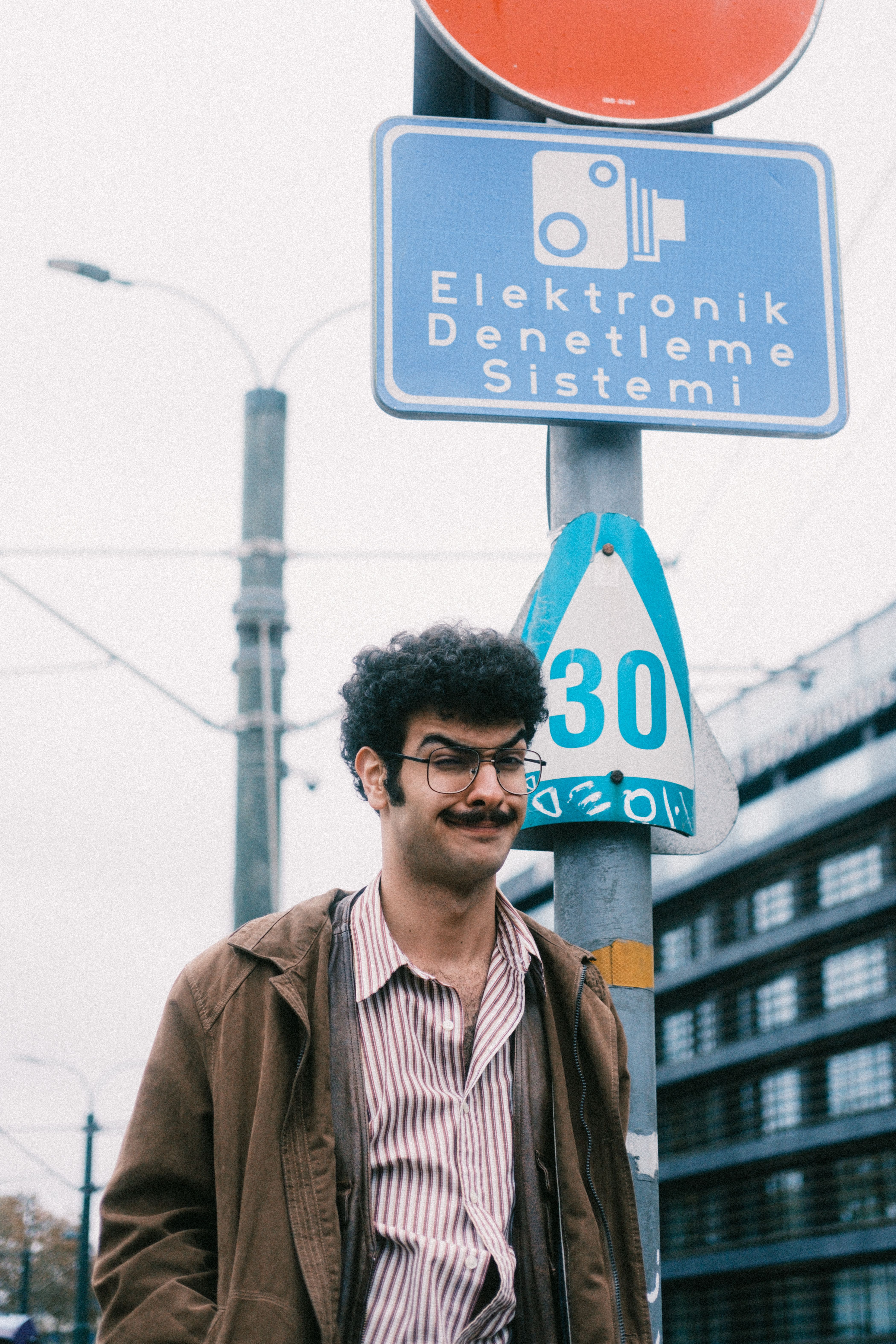 Smiling man with moustache in casual clothes stands by traffic sign in city.