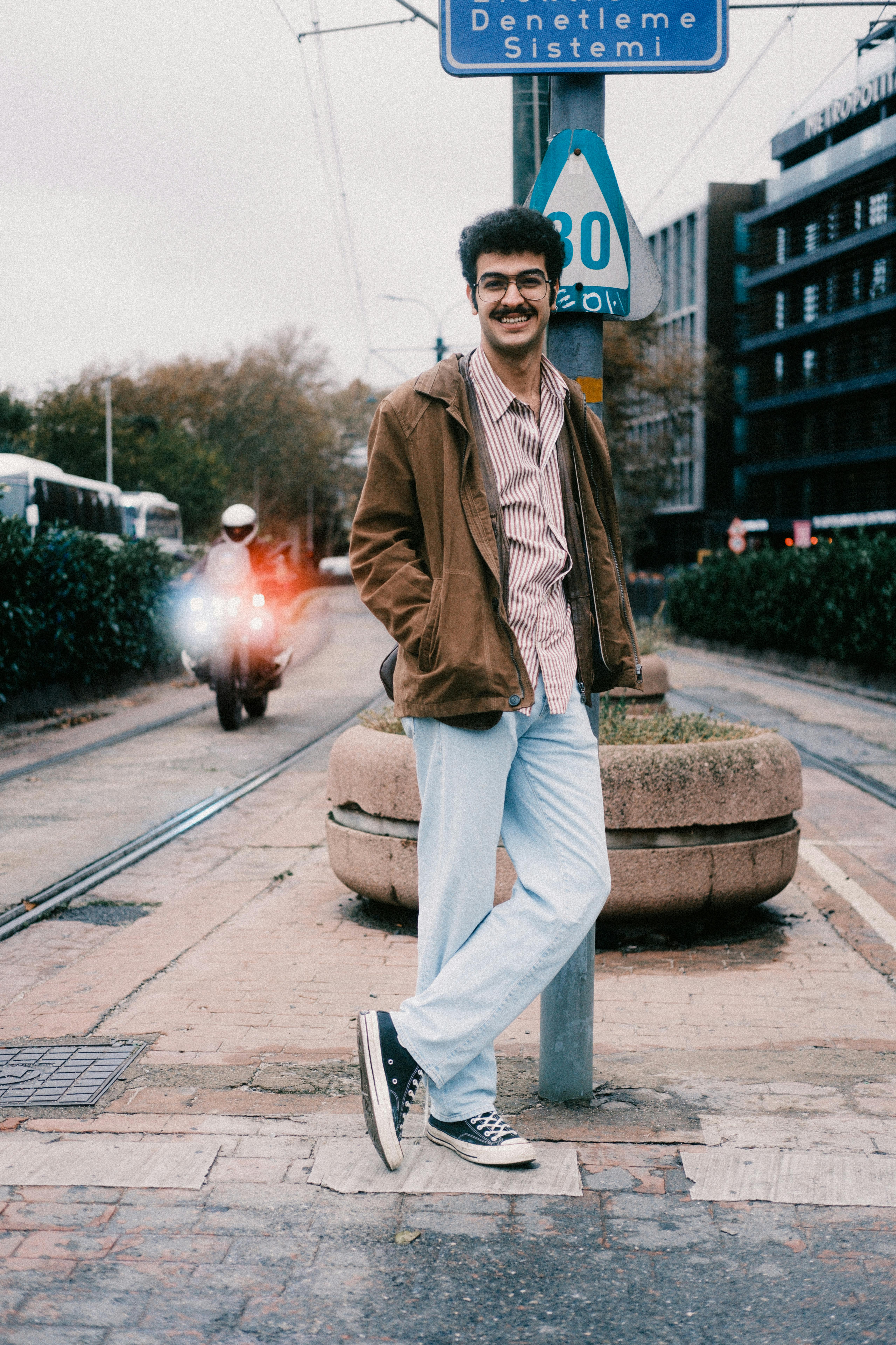 Young man in casual attire smiling by a city street with tram rails.