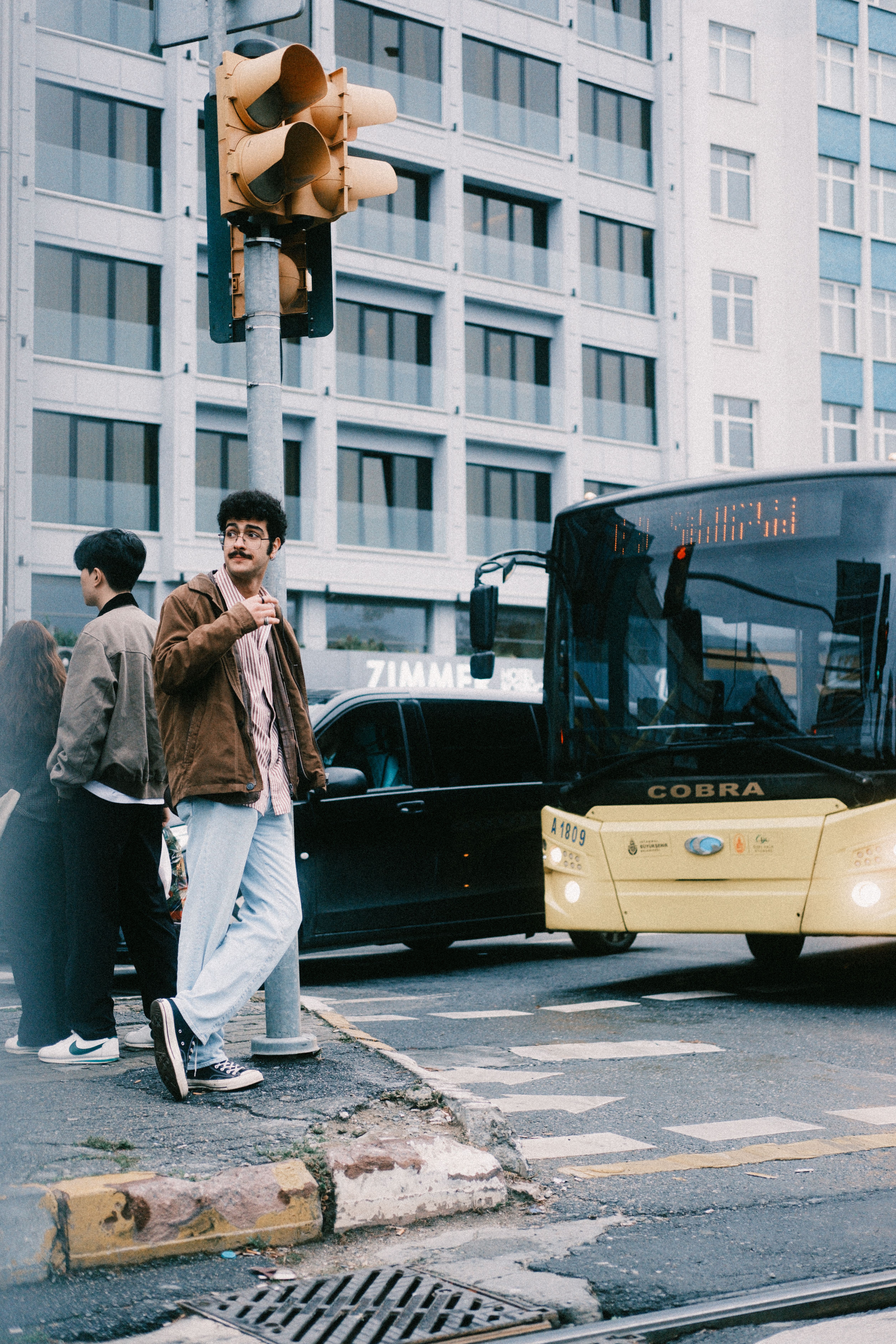 Busy urban street with pedestrians crossing and a yellow bus in the background.