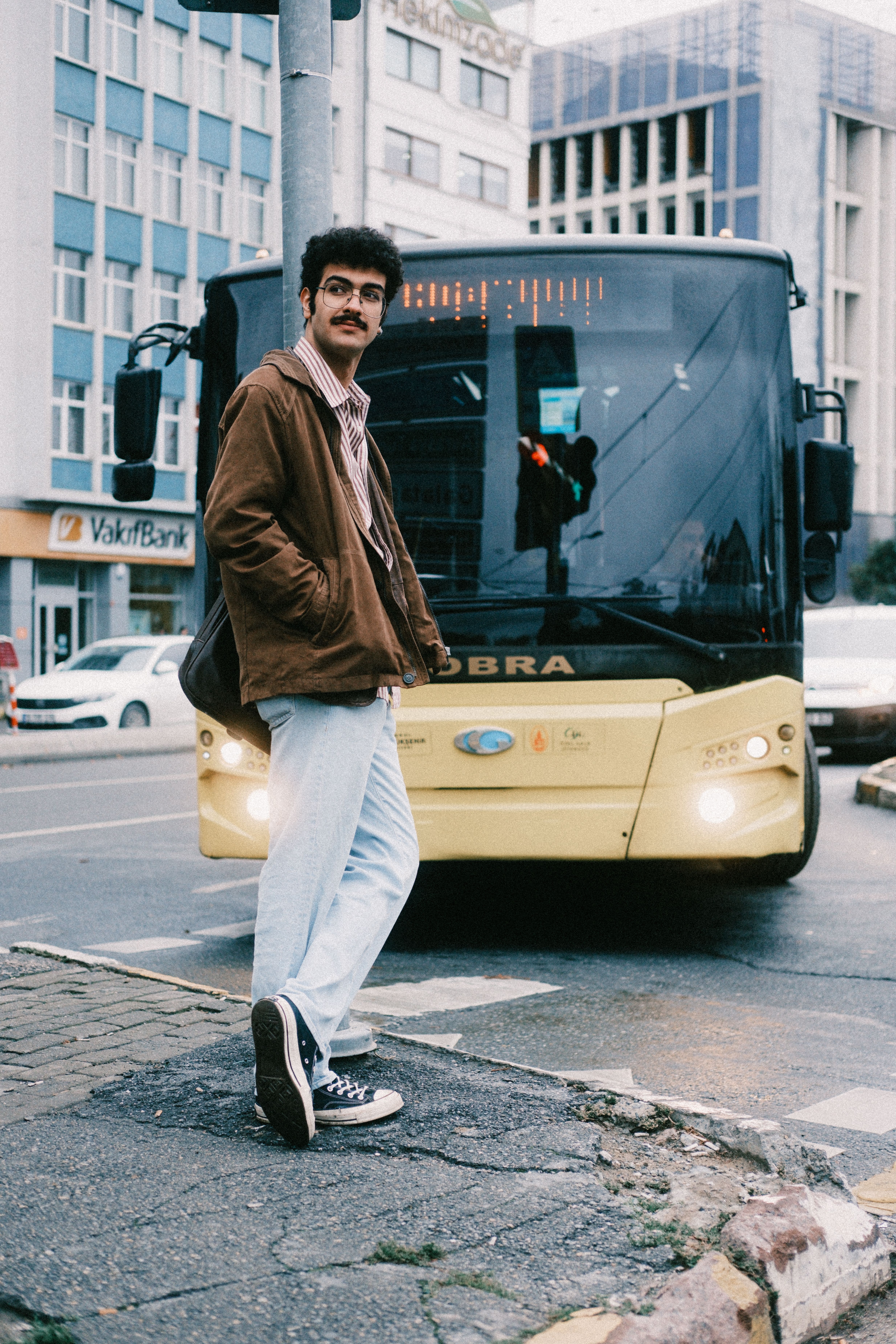 Man standing on city street near bus, capturing urban lifestyle.