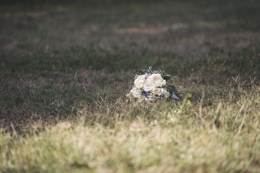 A delicate white rose bouquet gently placed on grassy lawn under soft sunlight, perfect for weddings.
