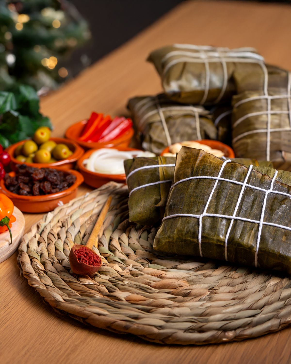 Tamales wrapped in banana leaves surrounded by peppers, olives, and spices on a festive table setting.