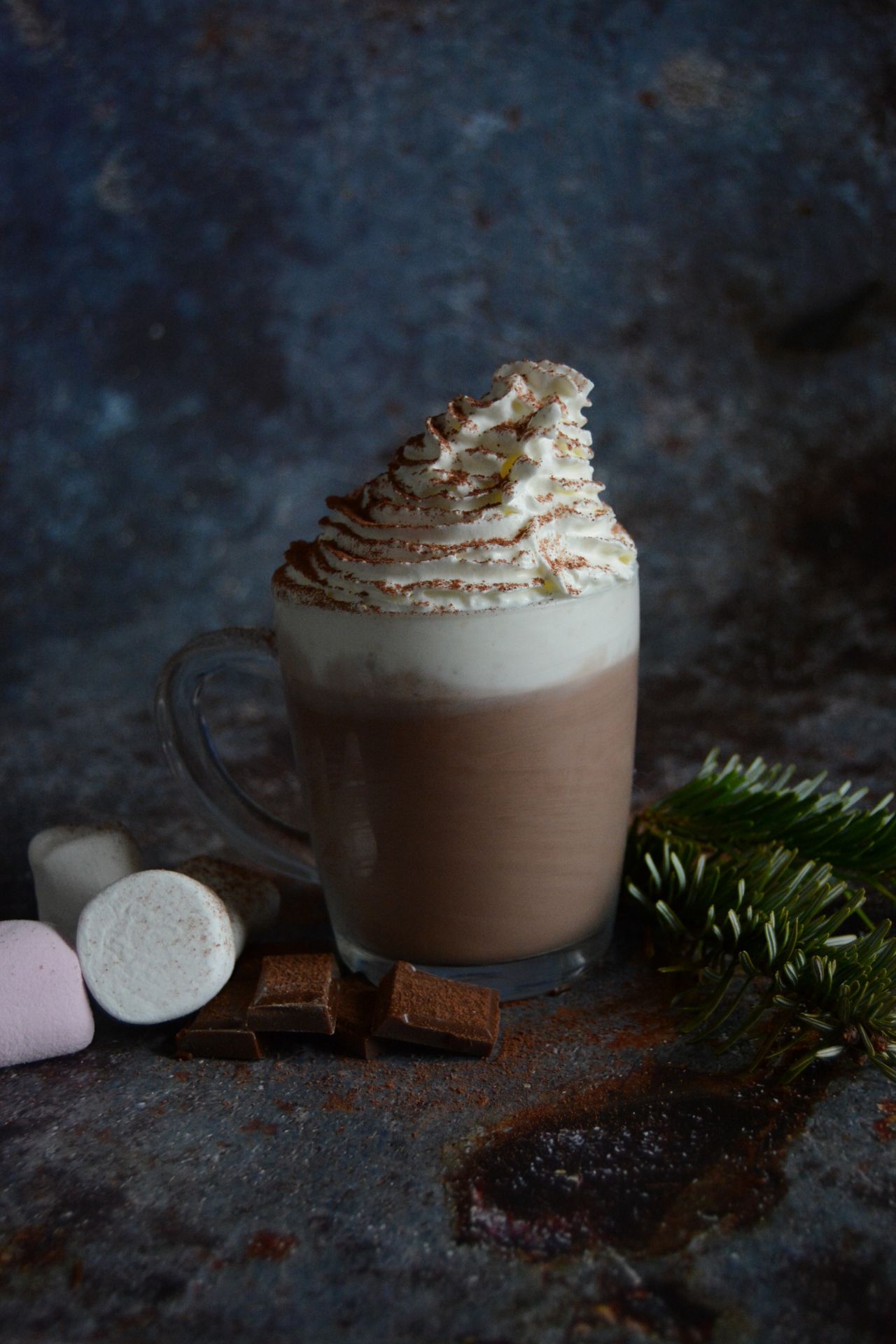 Glass mug of hot chocolate topped with whipped cream and cocoa powder