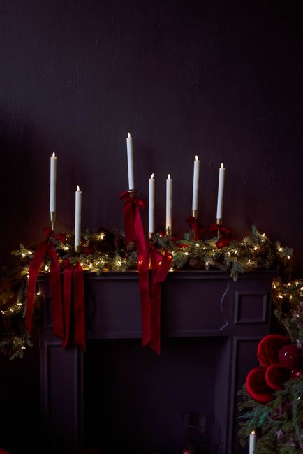 Festive Christmas mantel decor with candles, garland, and red ribbons, creating a warm holiday ambiance.