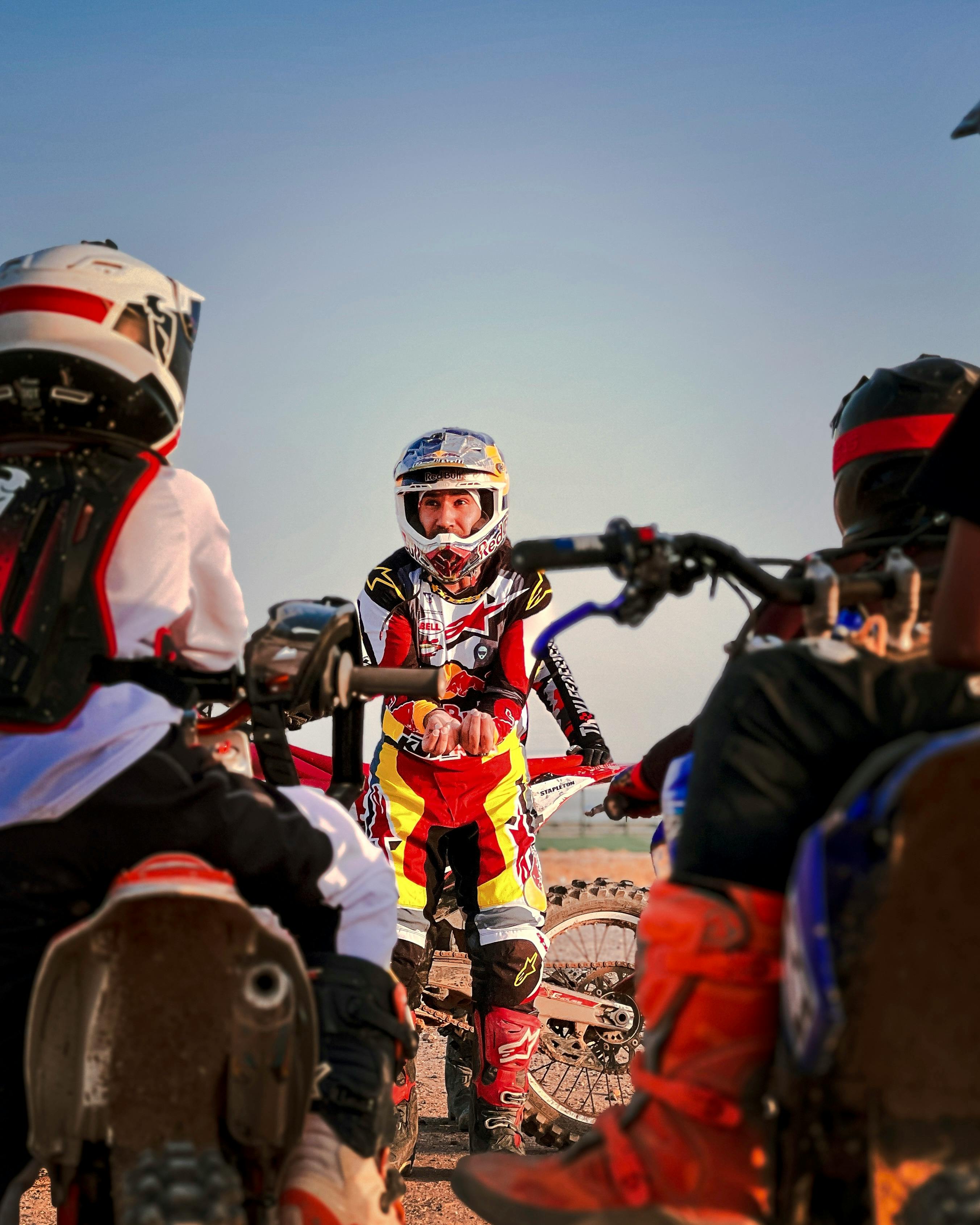 A group of young motocross enthusiasts gather outdoors with their dirt bikes, learning from a guide.