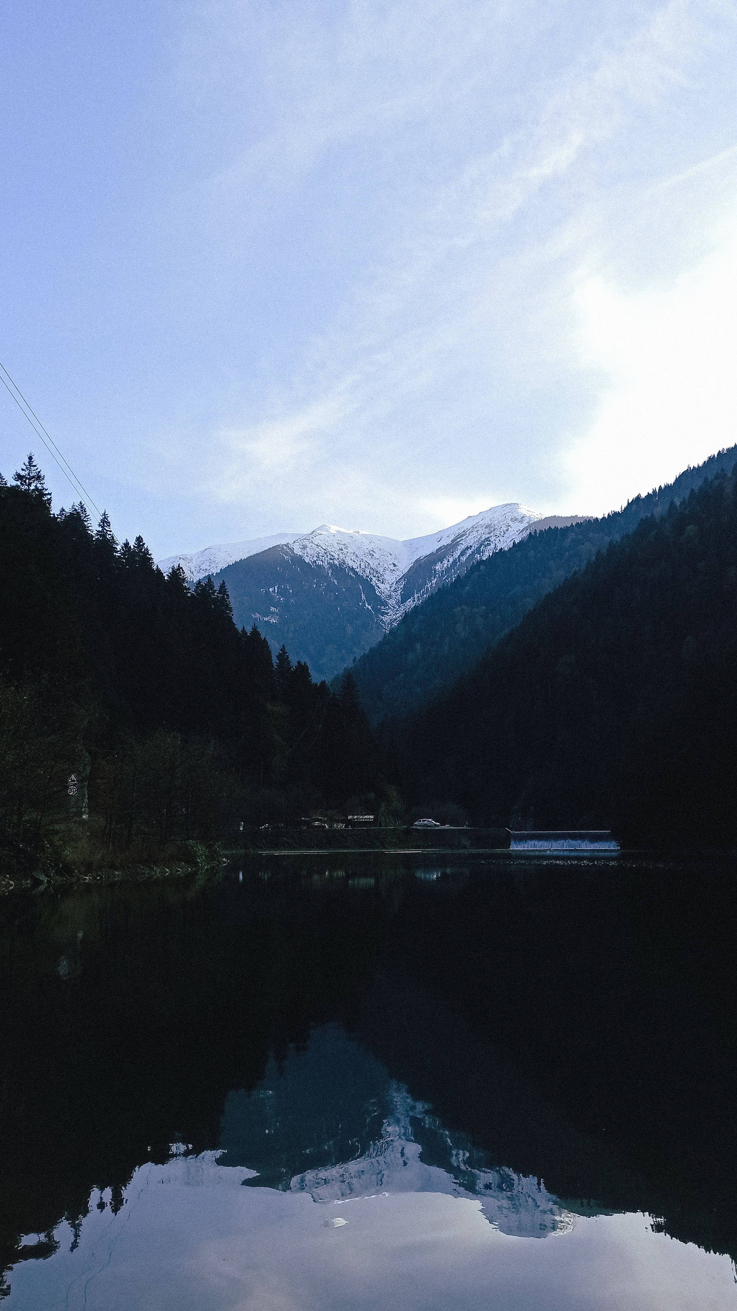 Peaceful mountain lake with snowy peaks and dense forest under a clear sky.